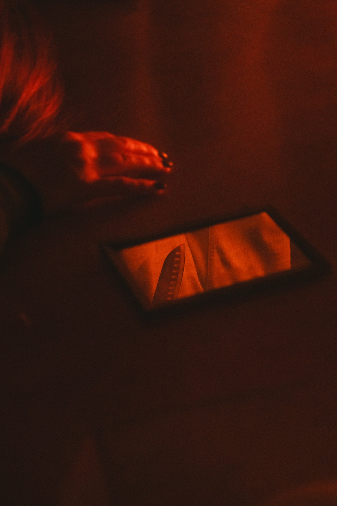 A hand and mirror reflect in red light.