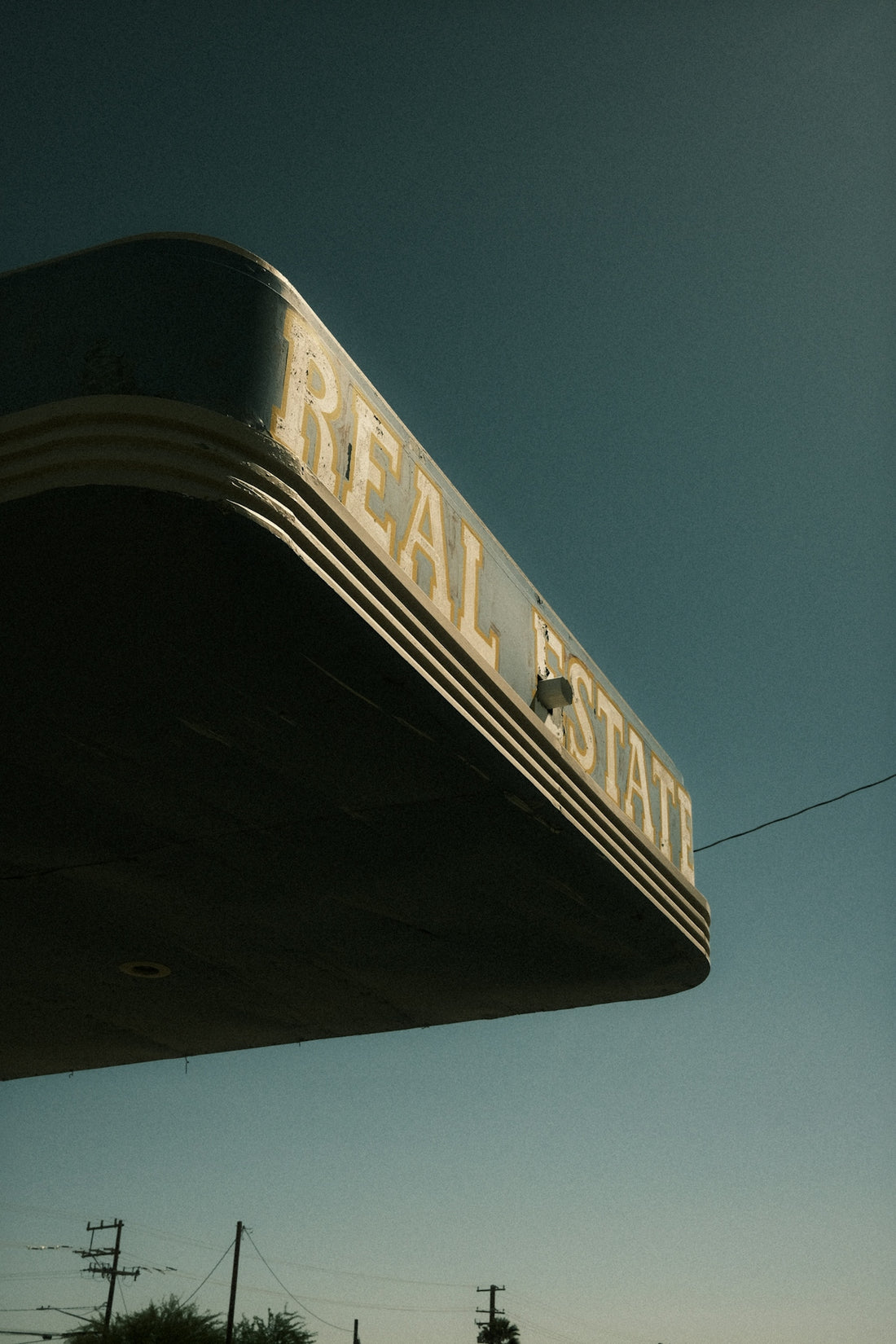 Old real estate sign stands against a clear sky.